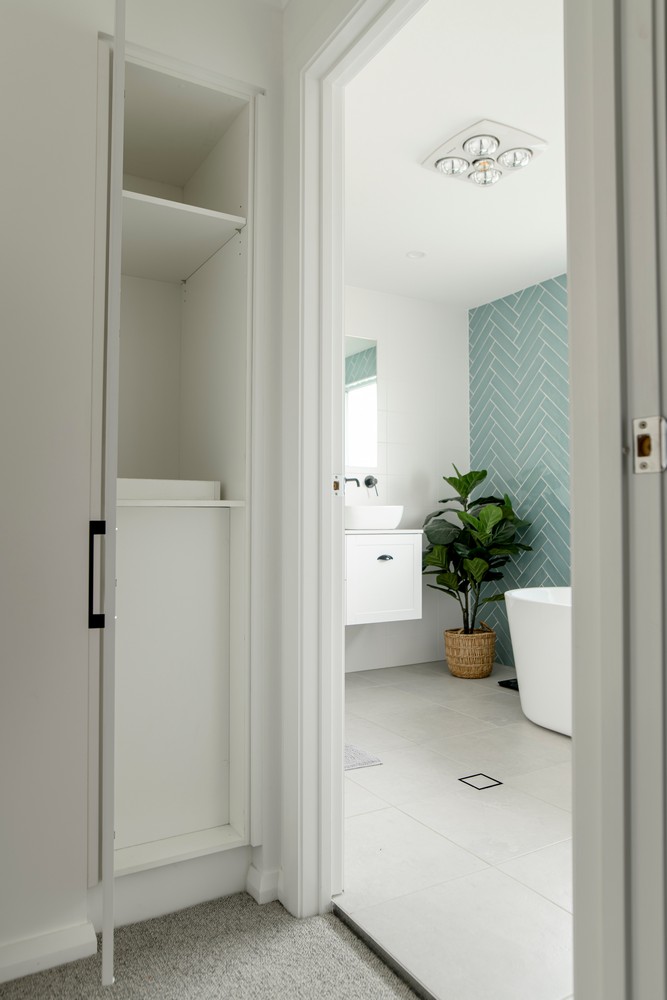 Bright bathroom featuring a white freestanding tub, herringbone teal tiles, potted plant, and a closet space visible through an entryway.