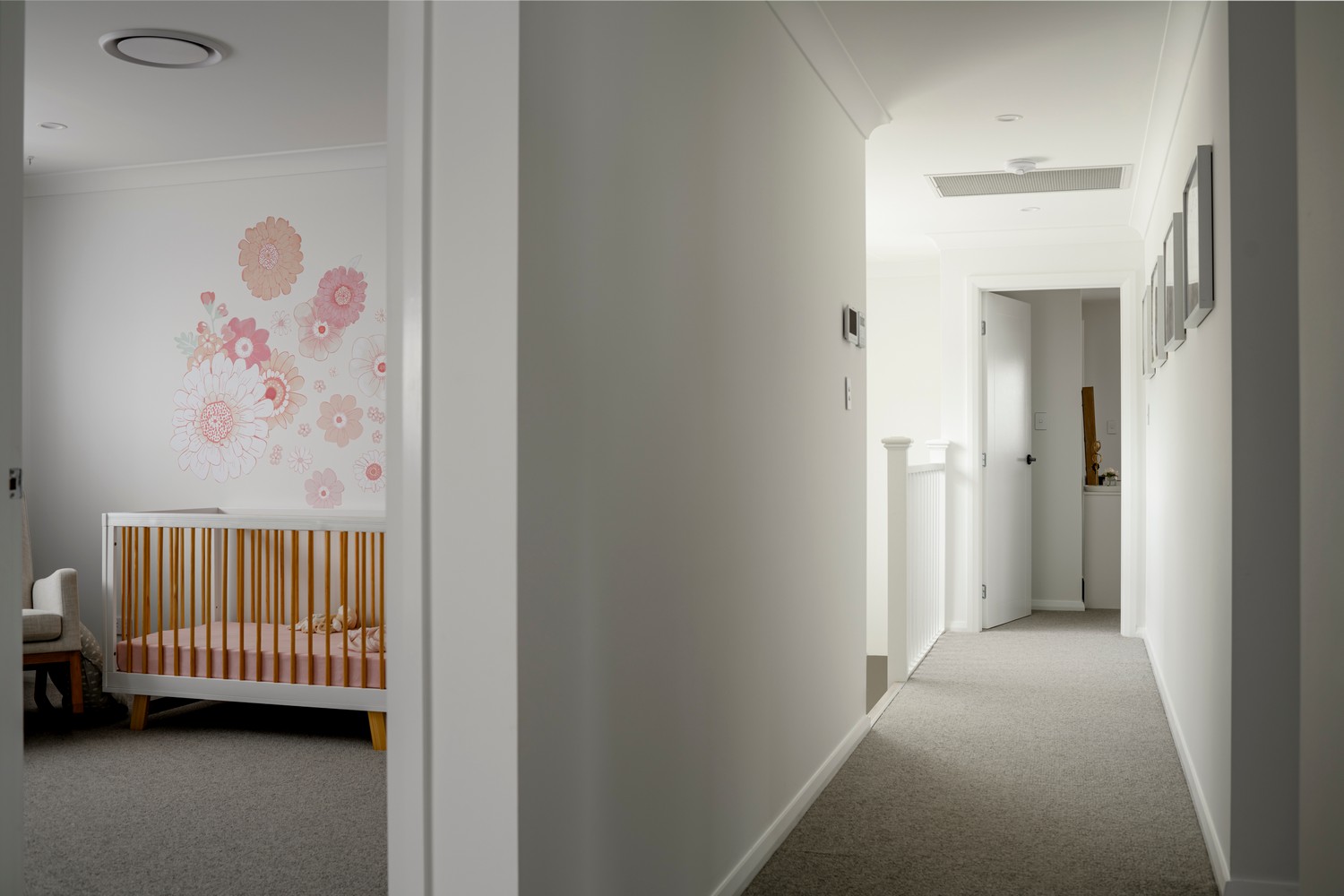 Light and airy hallway featuring a stylish wooden cot, pastel floral wall art, and neutral-coloured walls and carpet.