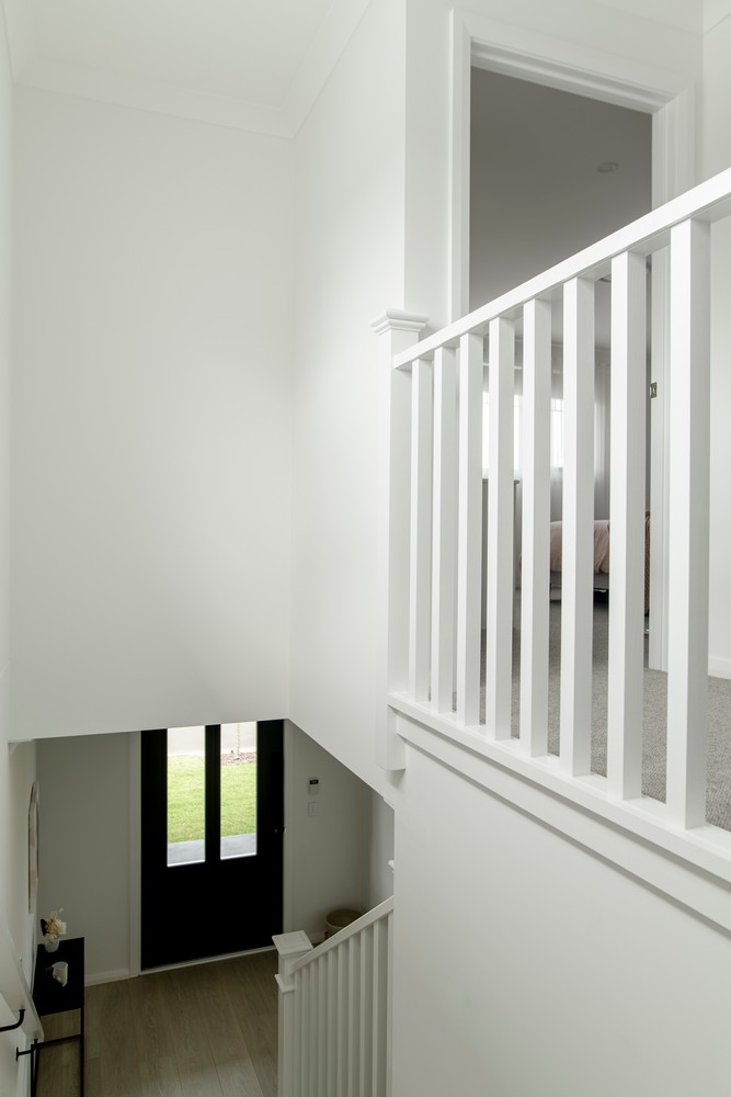 Bright, modern hallway with a white staircase and railing, leading to a black front door. Natural light filters in from upper rooms.