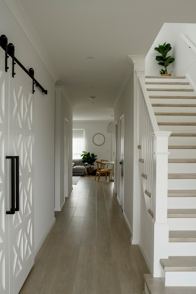 Bright hallway featuring a staircase, wooden flooring, and a decorative plant. Light grey walls complement sliding barn doors.