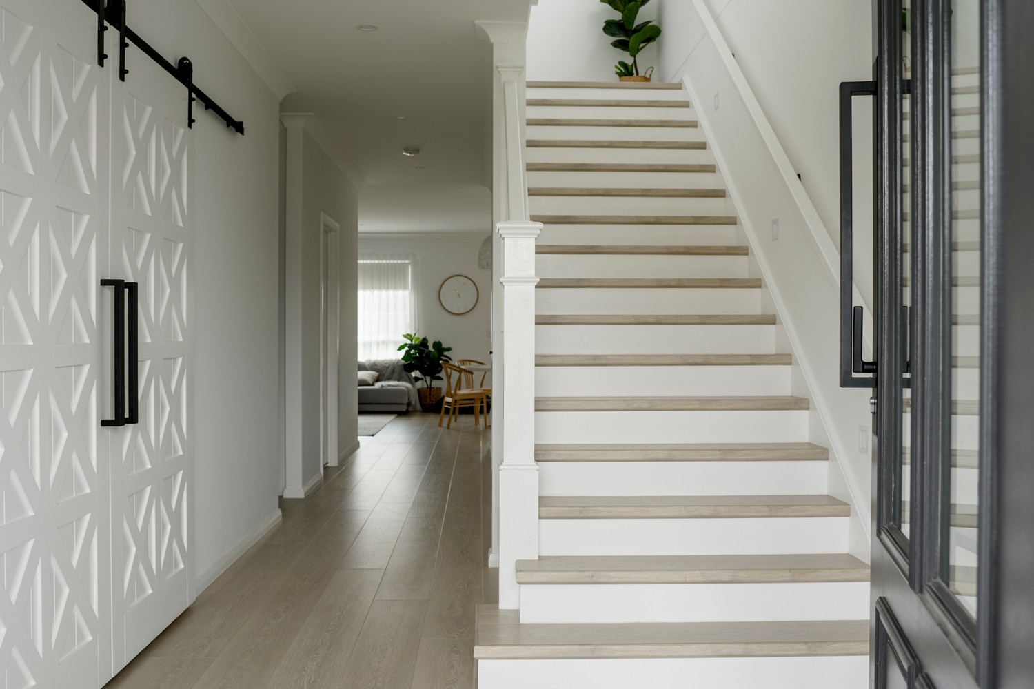 Bright interior showcasing a modern staircase, light wood flooring, and decorative plants, leading to a spacious living area.