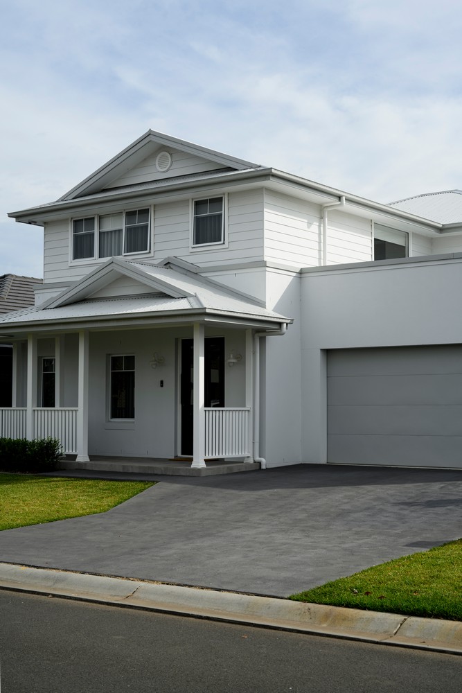 Modern two-storey white house with a gabled roof, front porch, and a grey driveway, set against a cloudy sky.