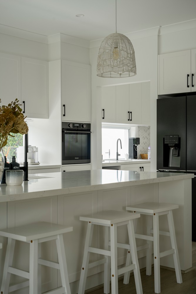 Modern kitchen with white cabinetry, a marble countertop, three wooden stools, and a pendant light, creating a bright and inviting space.