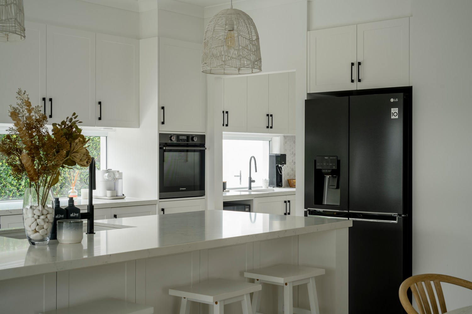 Modern kitchen with white cabinetry, black fridge, a marble island, and decorative vase of dried flowers, creating a bright, inviting space.