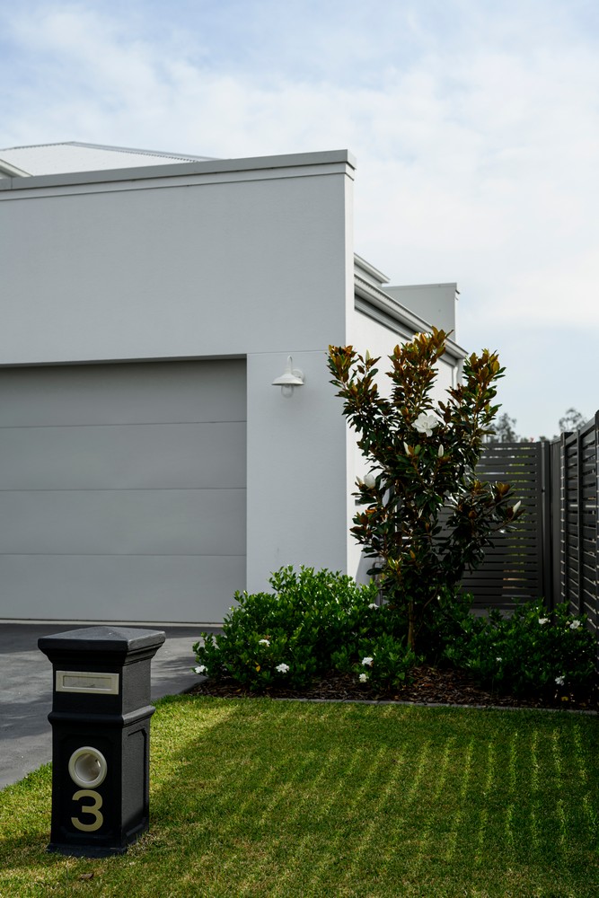 Modern house exterior featuring a grey garage, a mailbox with the number 3, a small magnolia tree, and well-maintained green grass.