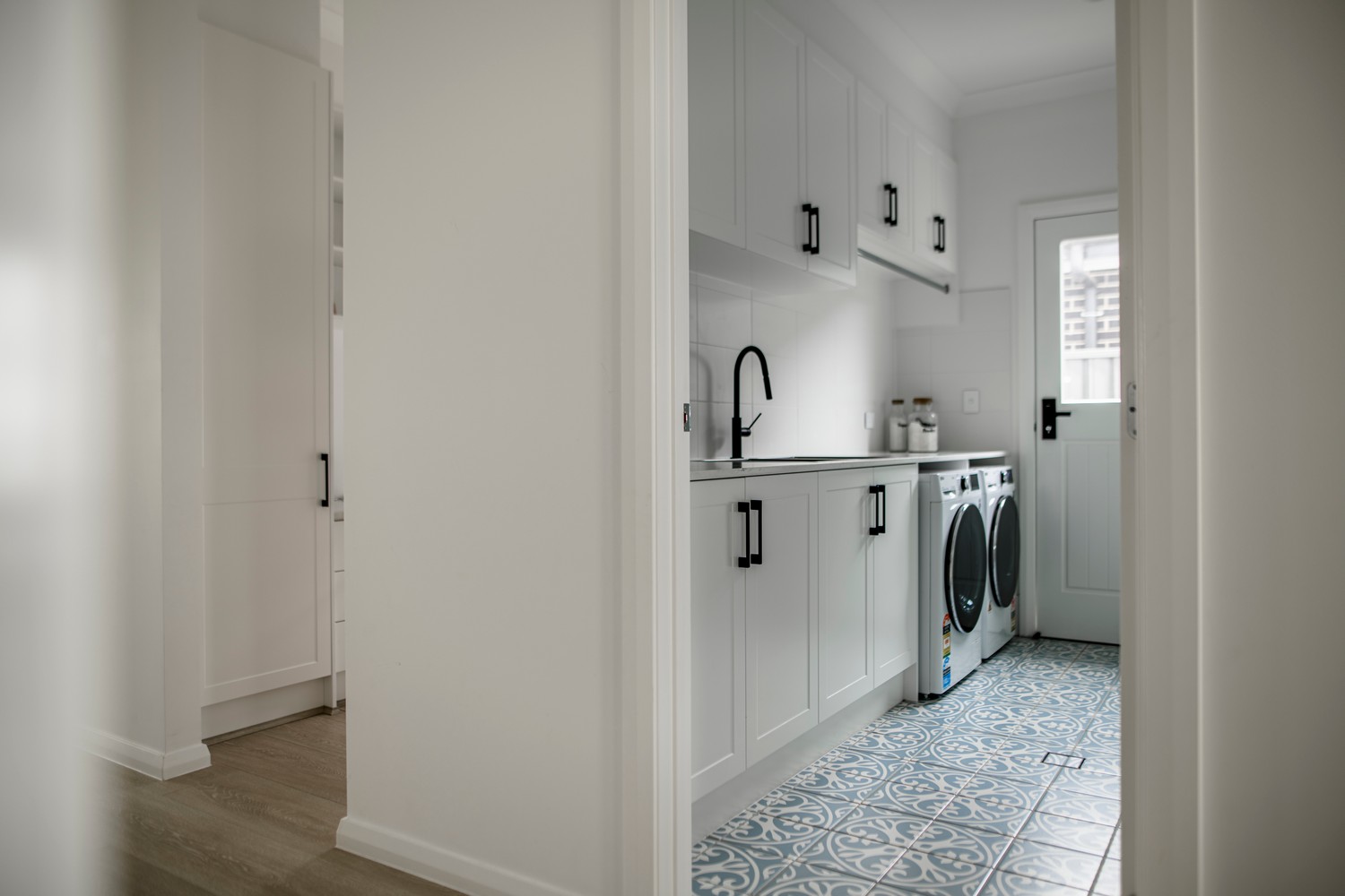 Bright laundry space with white cabinetry, modern appliances, and patterned blue tiles, creating a clean, inviting atmosphere.