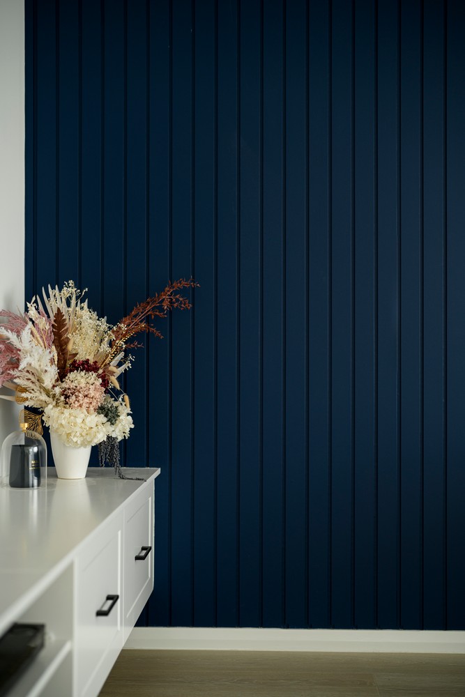 A white cabinet with black handles under a deep navy blue wall, adorned with a stylish arrangement of dried flowers in a vase.