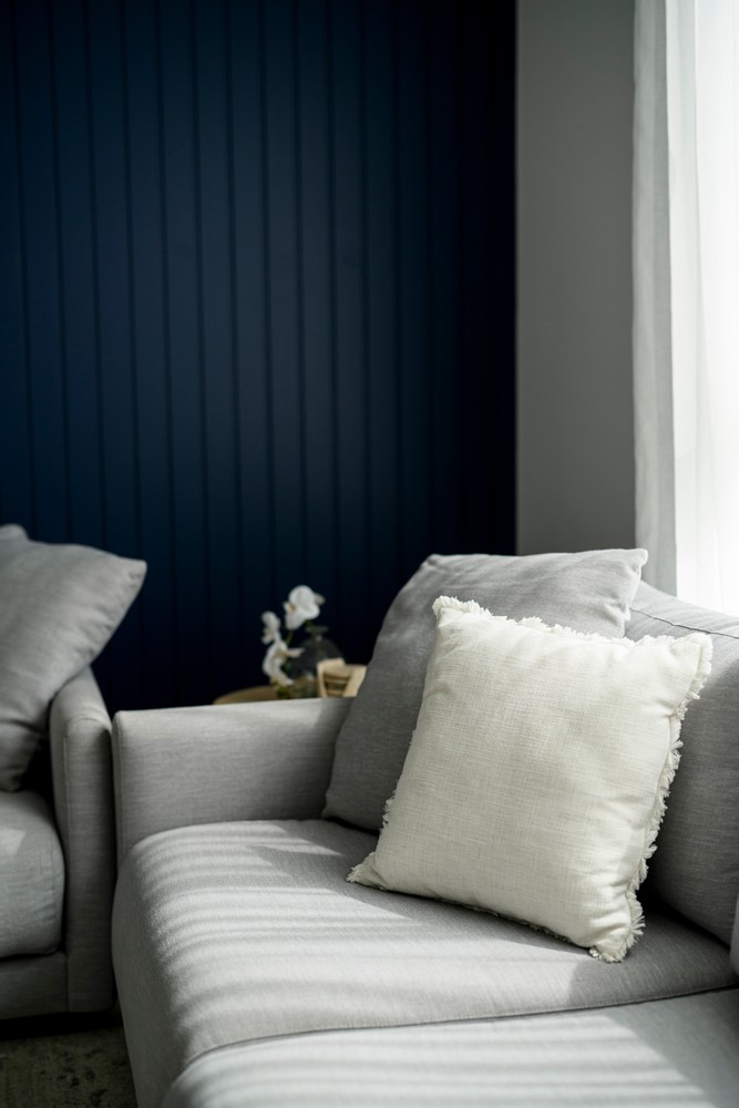A grey sectional sofa with a textured white cushion set against a deep blue paneled wall, featuring soft natural light.