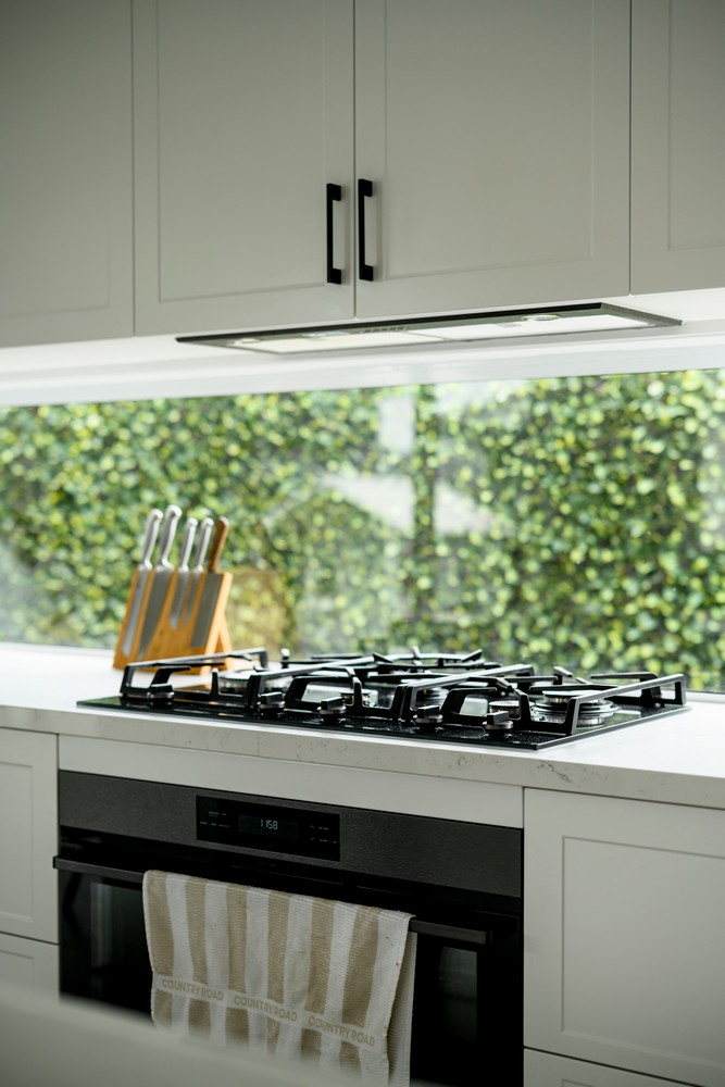 Modern kitchen featuring a sleek black gas stove, white cabinetry, and a knife block, with greenery visible through a large window.