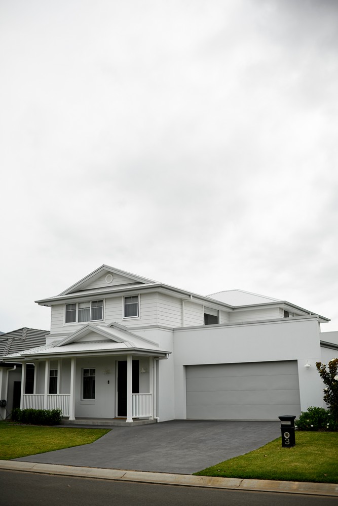 Modern two-storey white house with a front porch, large windows, and a grey driveway, set against a cloudy sky.