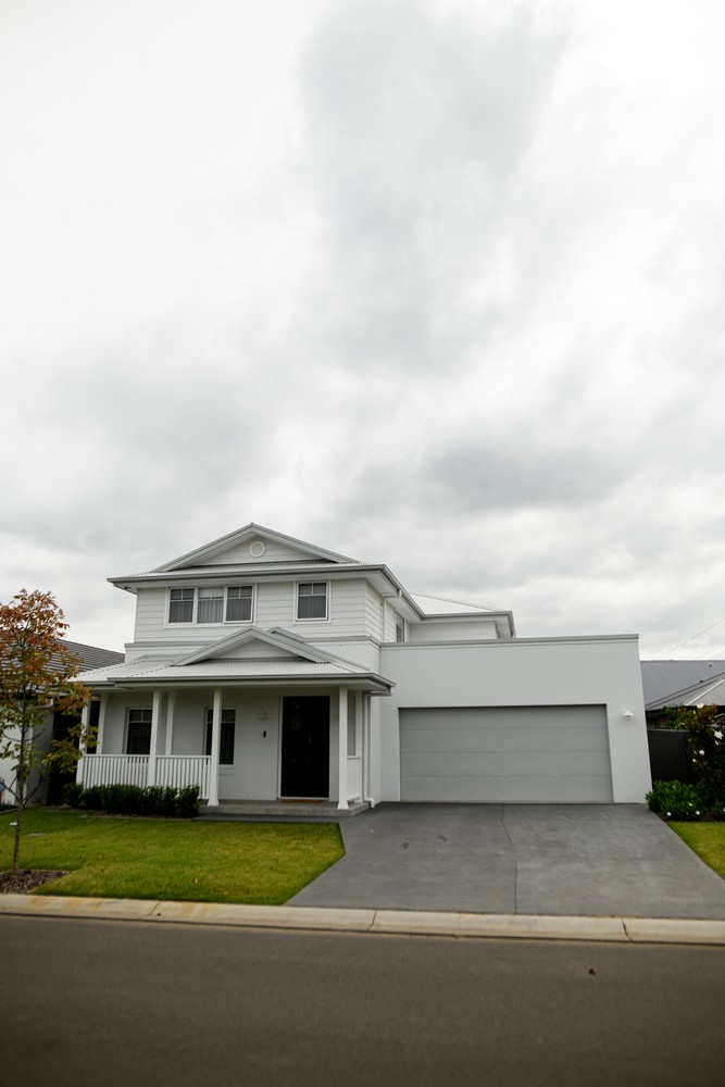 Modern two-storey white house with a grey garage, set on a green lawn under a cloudy sky.