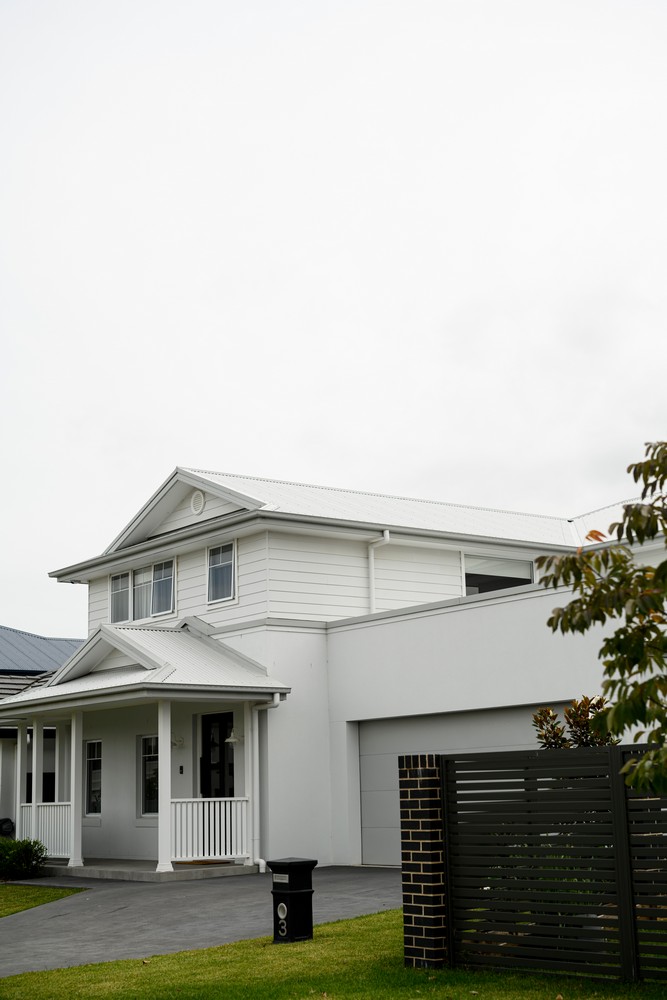 Modern two-storey house with a white exterior, wrought iron details, and a neatly manicured lawn, featuring a grey driveway and fence.