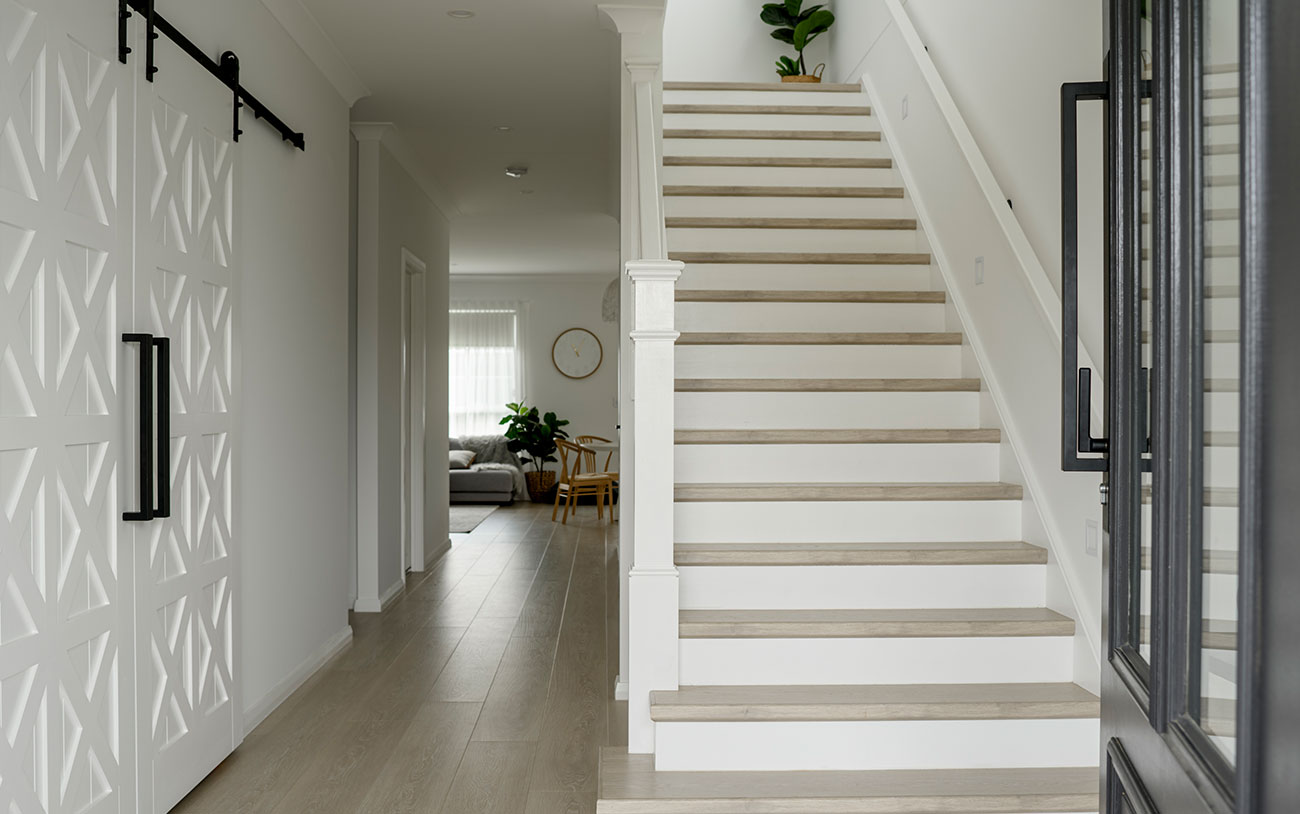 Bright, modern hallway featuring a white staircase, decorative sliding doors, and a view into a light-filled living area.