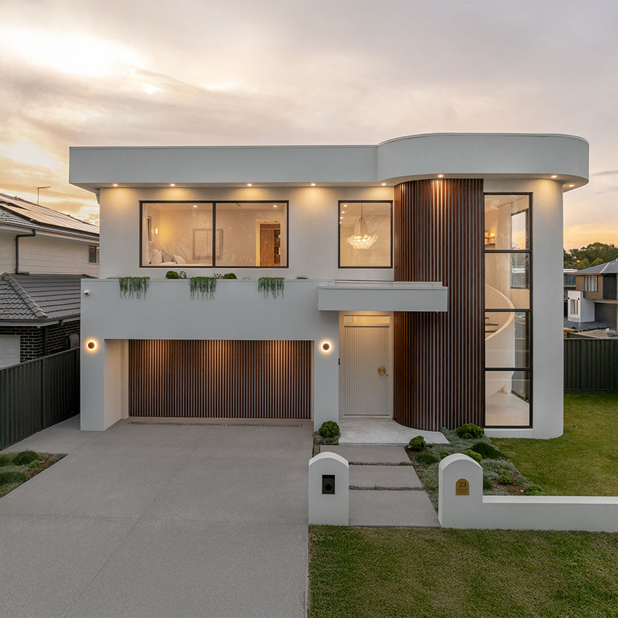 Modern white and timber house with large windows, elegant entrance, and manicured lawn, set against a soft evening sky.