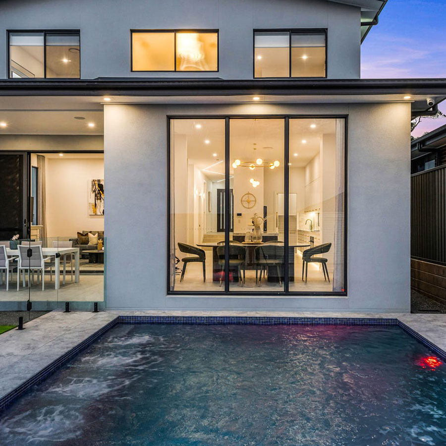 Modern home exterior featuring large glass windows overlooking a pool, with a stylish outdoor living area and contemporary furnishings.