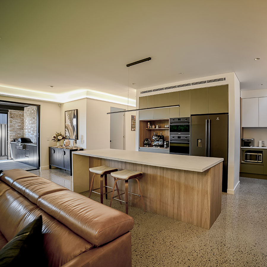 Modern kitchen with a sleek island, minimalist cabinetry in muted tones, and a spacious lounge area with a brown leather sofa.