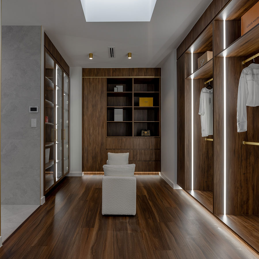 Modern interior featuring warm wooden cabinetry, built-in shelving, and illuminated wardrobes. Soft lighting enhances the sleek, minimalist design.