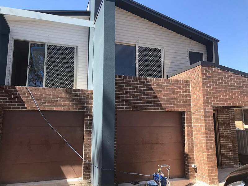 Contemporary two-storey home façade featuring a mix of white cladding and dark blue accents, with brick garages at the ground level.