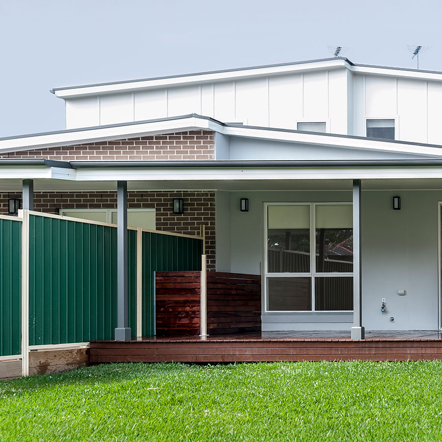 Modern duplex in Gledswood Hills featuring brick and cladding exterior, green fences, and a wooden deck on a grassy lawn.