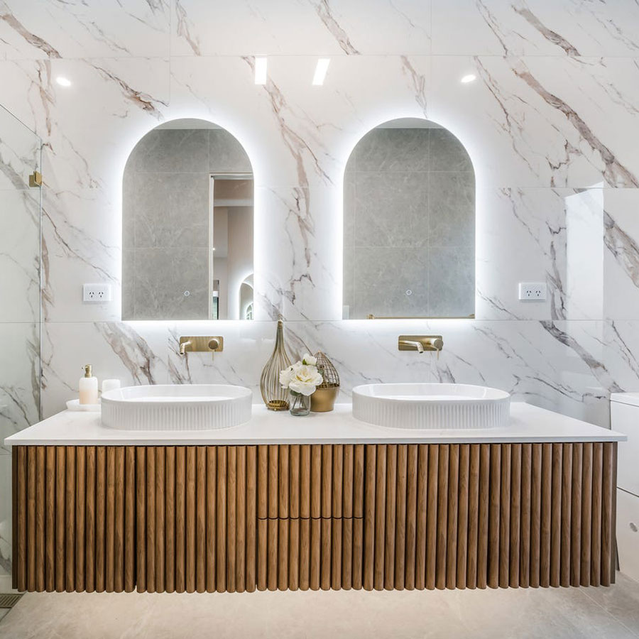 Elegant double vanity featuring a marble backsplash, two round basins, and backlit mirrors, complemented by a textured wooden cabinet.