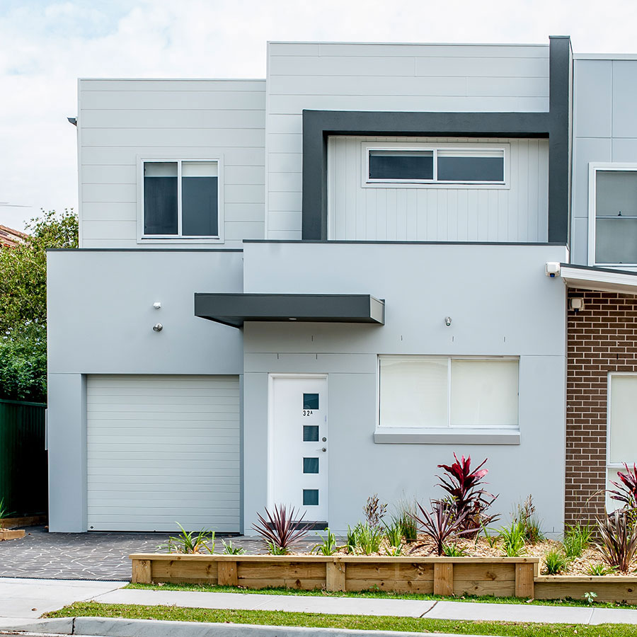 Modern duplex in Narellan featuring a sleek grey façade, a central entrance, and a garage, surrounded by landscaped greenery.