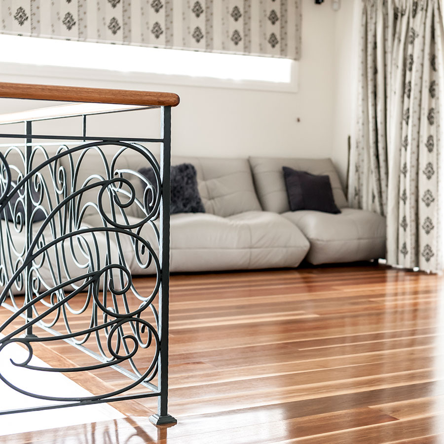 Elegant interior with a dark wrought iron railing, polished wooden flooring, and a light grey sofa adorned with cushions, complemented by patterned curtains.