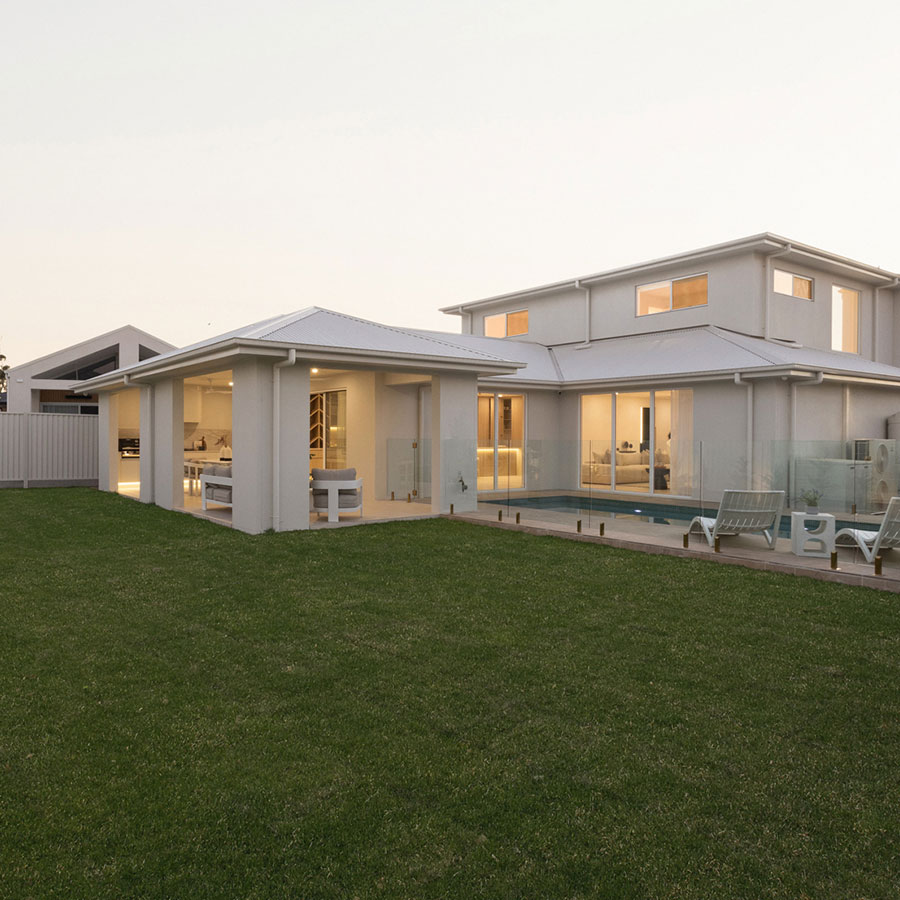 Modern single-storey home with a large outdoor area, featuring a glass pool, landscaped lawn, and sleek white architecture.