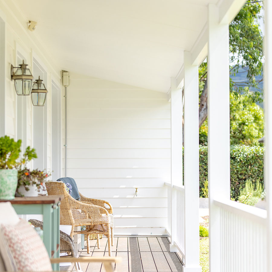 Bright, inviting porch with white walls, wooden floorboards, wicker chairs, and potted plants, offering a serene outdoor space.