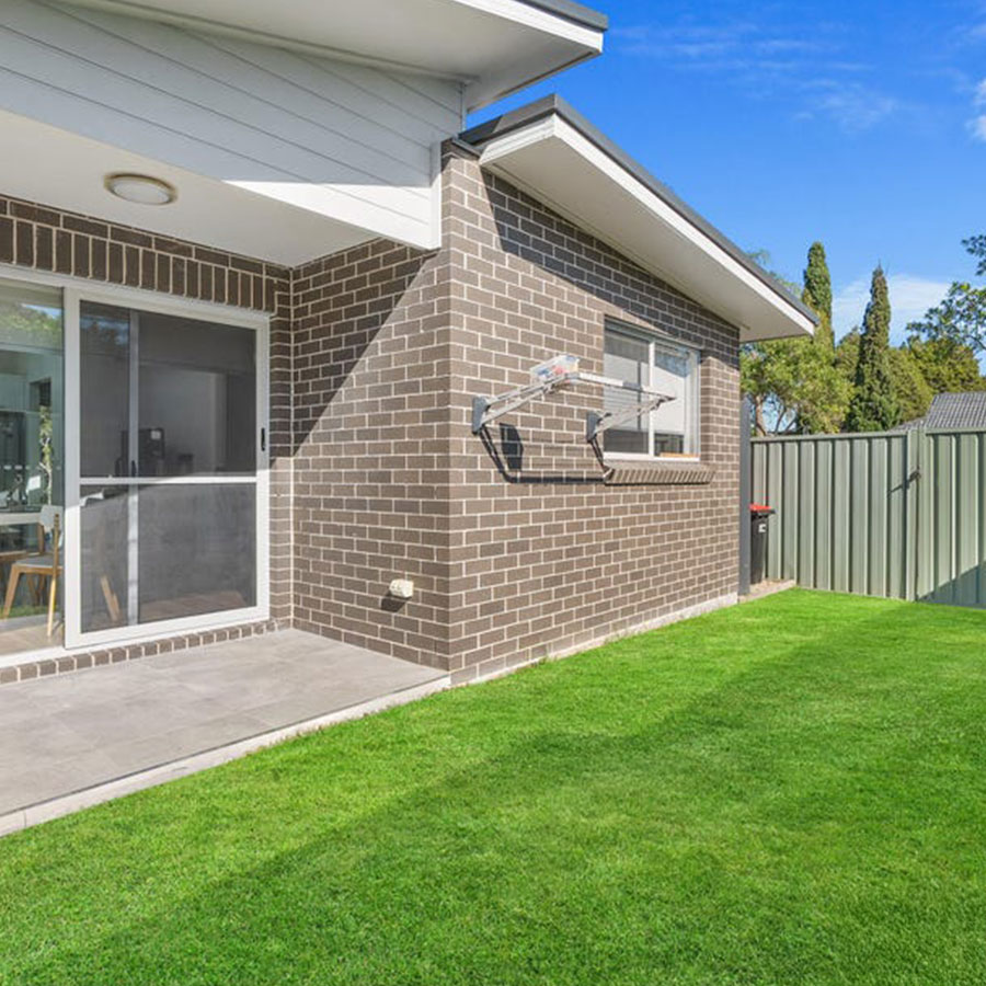 Modern bungalow with a brick exterior, sliding glass doors, and well-manicured lawn under a clear blue sky.