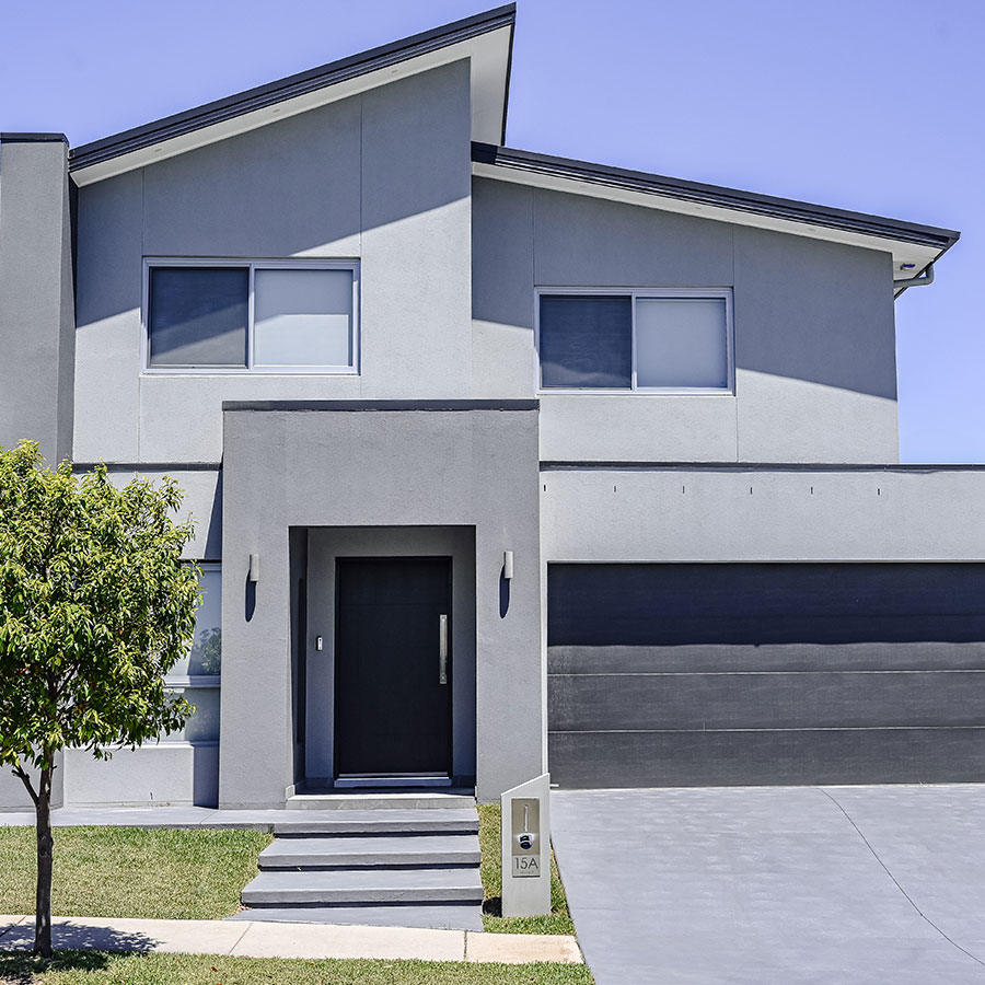 Modern grey house featuring a stylish entrance with a black door, large windows, and a complementary garage on a clear day.