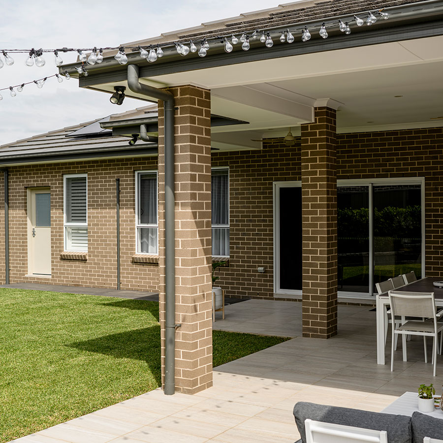 Modern home exterior in Gregory Hills, featuring a brick façade, outdoor seating area, and decorative string lights above a grassy yard.