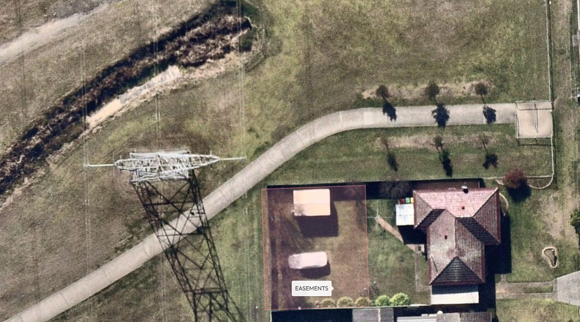 Aerial view of a residential area featuring a marked easement section, a house, a pathway, and a power line nearby.